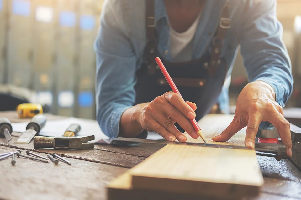 Artisan en atelier travaillant sur établi en bois, portant tablier et chemise bleue