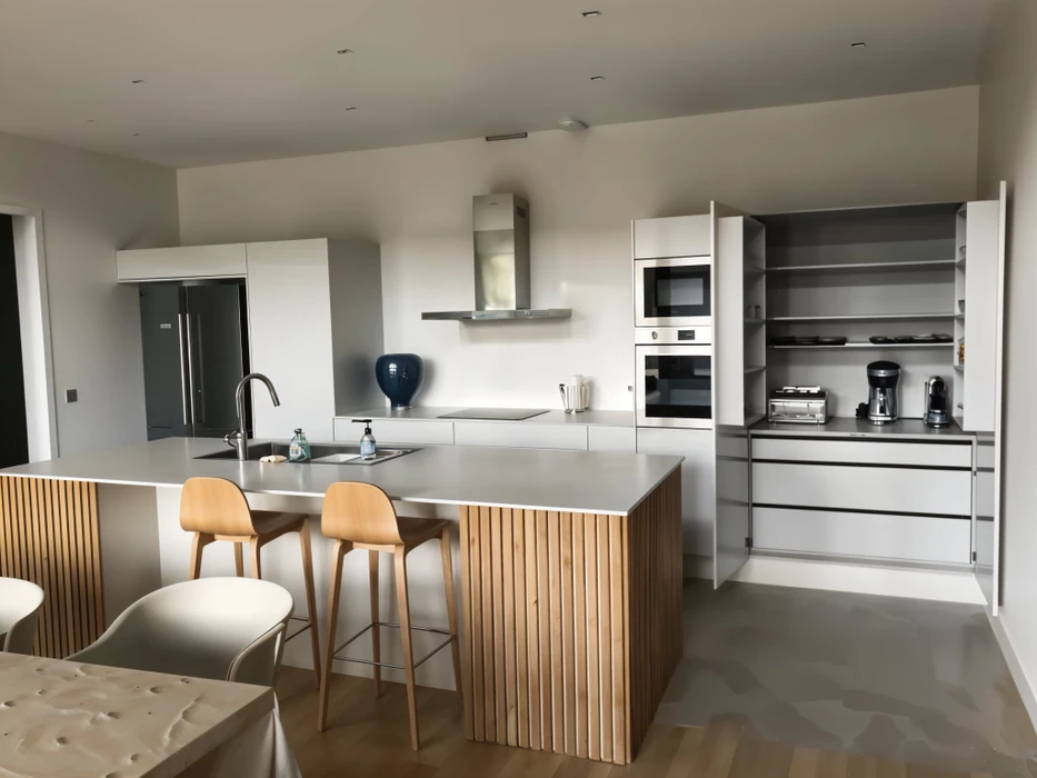 Cuisine moderne ouverte avec îlot central, deux personnes assises sur tabourets hauts en bois