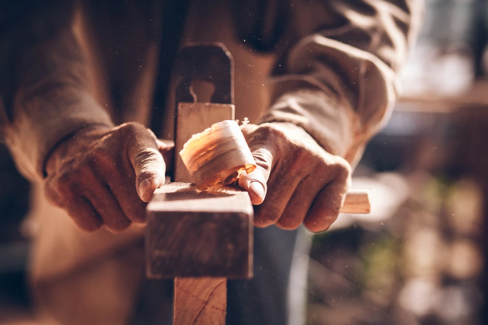 Artisan menuisier travaillant le bois dans son atelier, utilisant un rabot à main pour façonner une pièce de bois massif